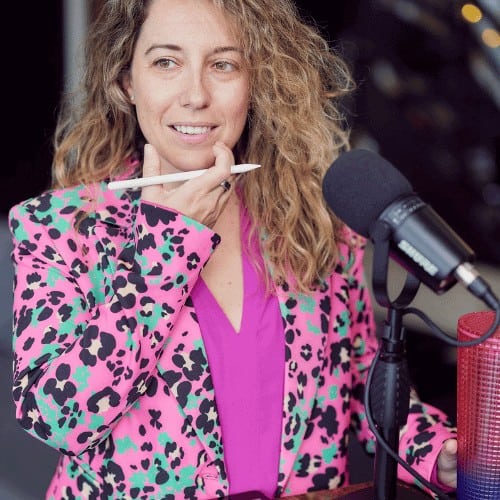 Nikki is in a pink patterned jacket with a pencil and microphone
